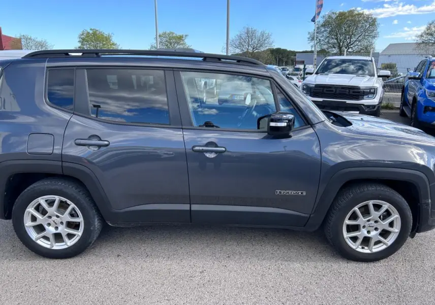 Jeep Renegade bleu foncé vu de profil côté gauche, avec jantes alliage 17 pouces et barres de toit noires.