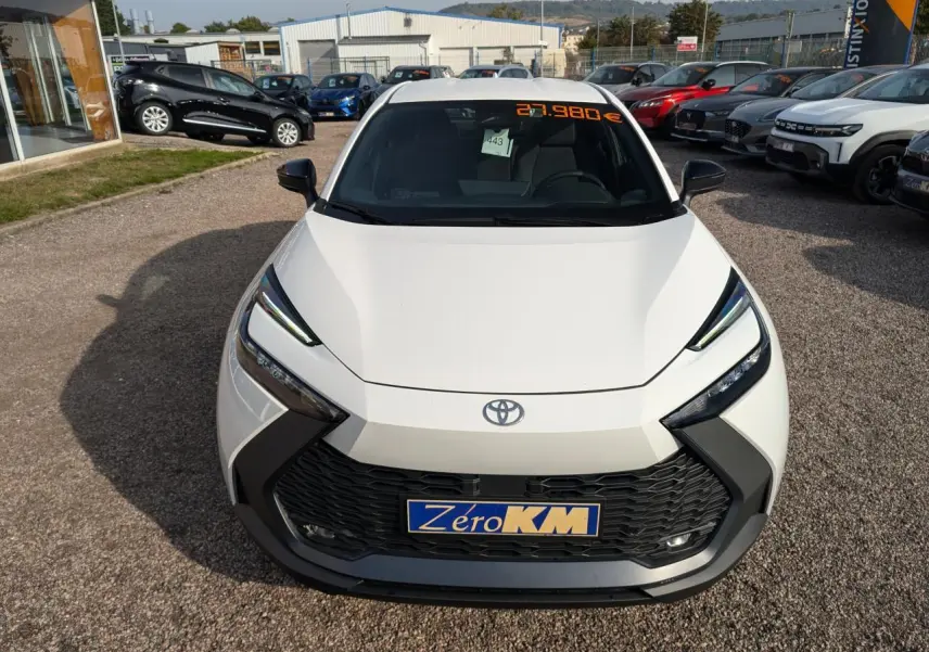 Vue avant d'un Toyota C-HR blanc 2024 hybride, avec calandre noire et phares LED fins, en concession extérieure.