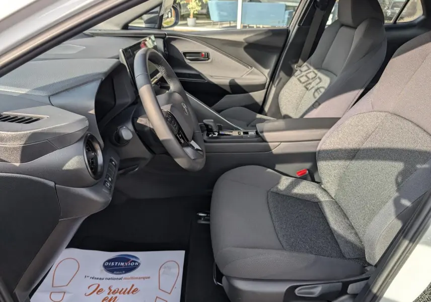 Intérieur du Toyota C-HR 1.8 Hybrid 2024 vu côté conducteur, sièges tissu gris et tableau de bord moderne.