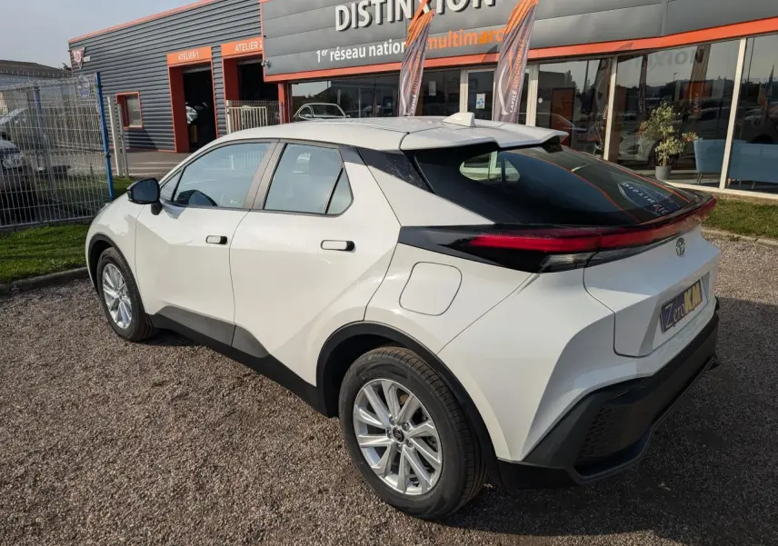 Toyota C-HR 1.8 Hybrid blanc vu en 3/4 arrière droit, avec feux arrière étirés et toit noir contrastant.