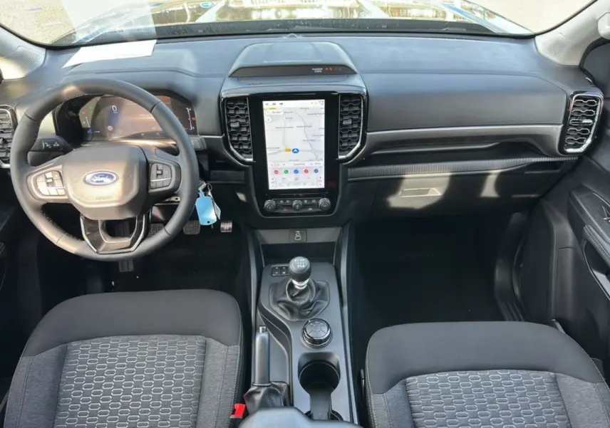 Vue intérieure frontale du Ford Ranger gris carbone 2025, montrant le tableau de bord avec écran tactile vertical et boîte manuelle.