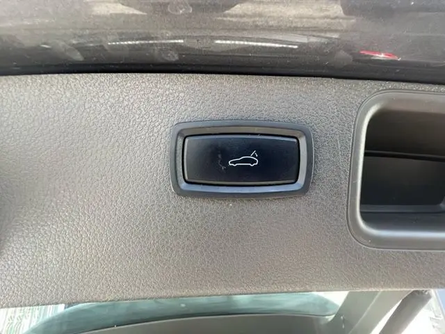Bouton noir d'ouverture du coffre sur la garniture intérieure grise du hayon d'un Porsche Macan gris diesel 2015.