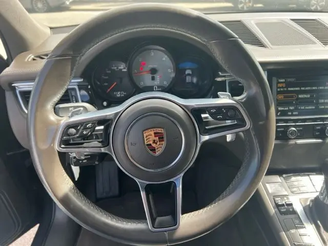 Vue rapprochée du volant en cuir noir du Porsche Macan gris 2015, avec tableau de bord et commandes visibles.
