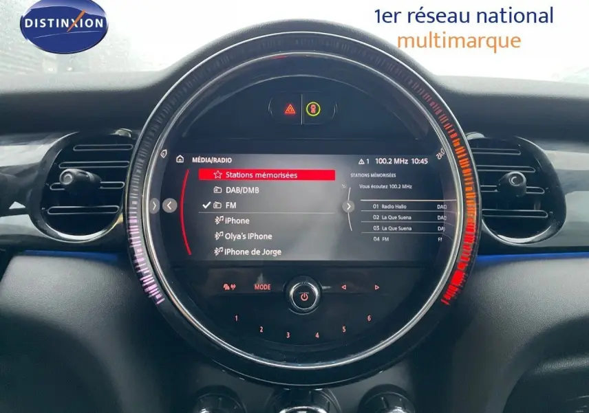 Affichage central circulaire du système multimédia de la MINI Cabriolet 2023, avec menu radio FM et connectivité iPhone visible.