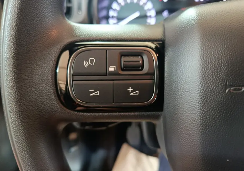 Gros plan sur les commandes multifonctions noires du volant de la Citroën C3 BlueHDi 100 BVM PLUS 2024.