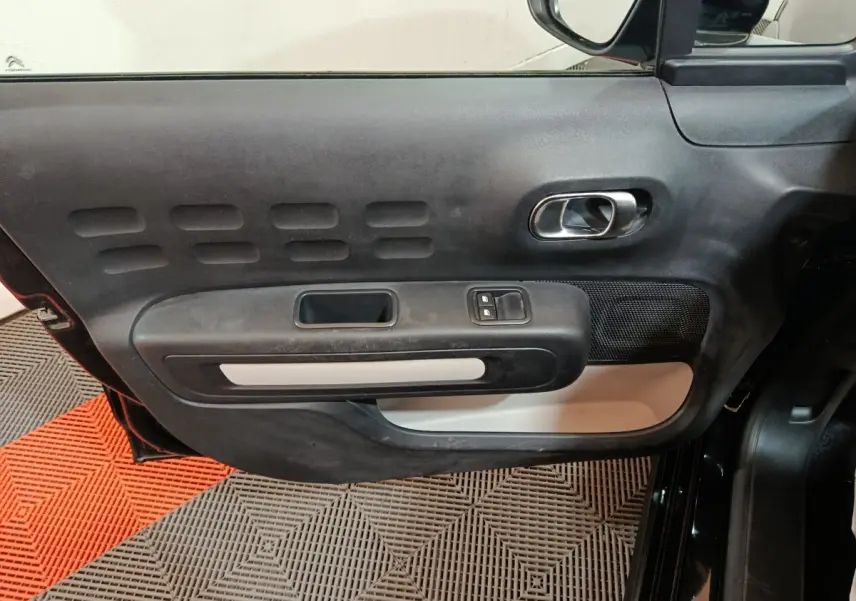 Vue intérieure côté gauche de la porte noire de la Citroën C3 2024 avec poignée chromée et commandes électriques.