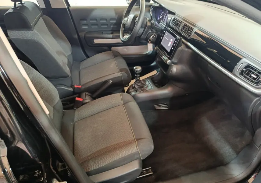 Vue intérieure côté conducteur de la Citroën C3 noire 2024, montrant sièges tissu, tableau de bord avec écran tactile et volant multifonctions.