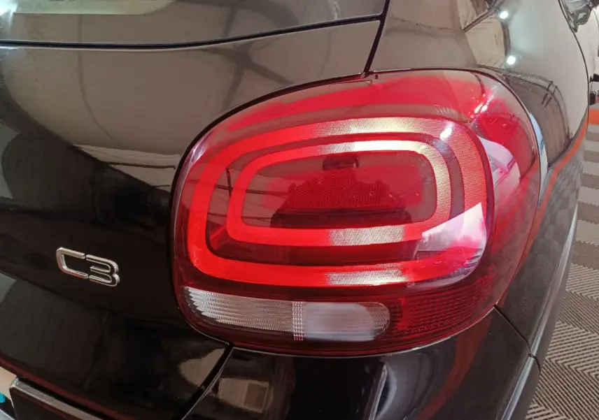 Gros plan sur le feu arrière droit rouge et blanc d’une Citroën C3 noire, avec logo C3 visible sur la carrosserie.