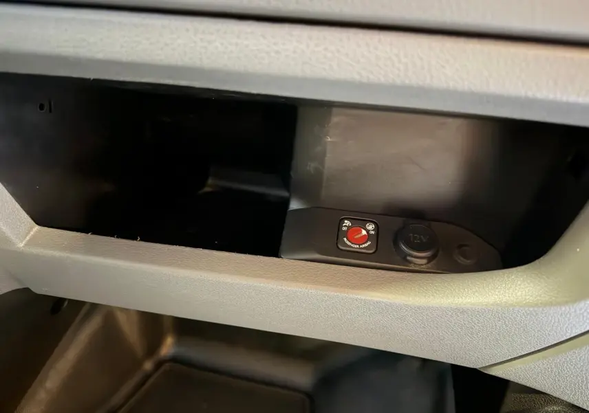 Gros plan sur la boîte à gants grise du Citroën Jumpy 2.0 BlueHDi 180, montrant un bouton de désactivation airbag et prise 12V.