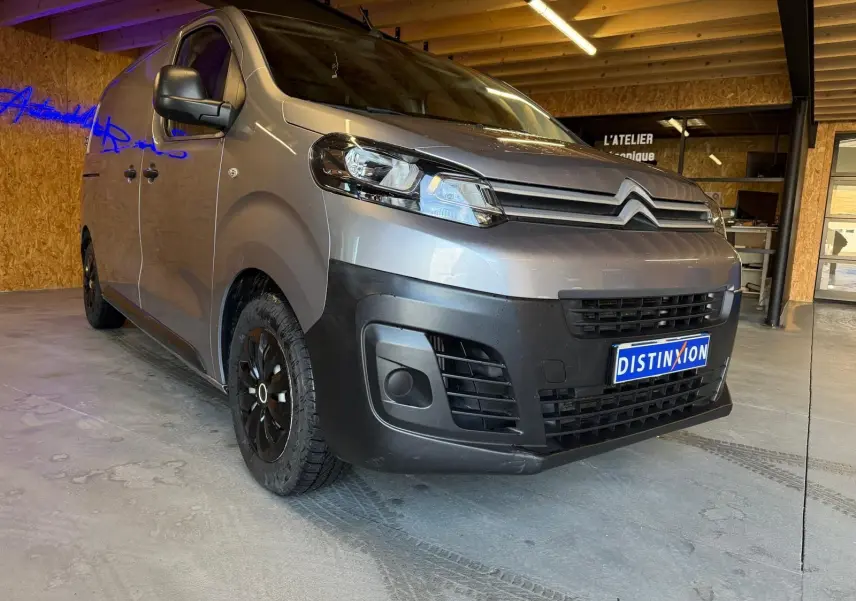 Vue 3/4 avant gauche d'un Citroën Jumpy gris métallisé 2022 avec calandre noire et jantes noires en intérieur d'atelier.
