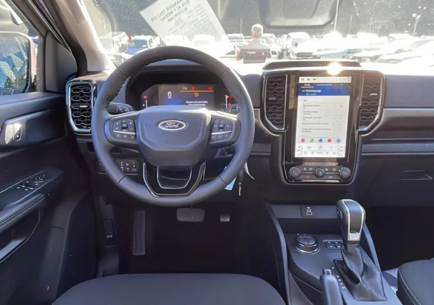 Vue intérieure avant du Ford Ranger 2025 avec tableau de bord noir, volant multifonctions et écran tactile vertical.