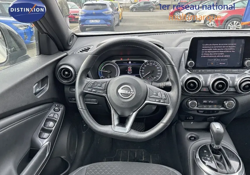 Vue intérieure du poste de conduite du Nissan Juke gris perle 2024, avec volant multifonction et écran tactile central.