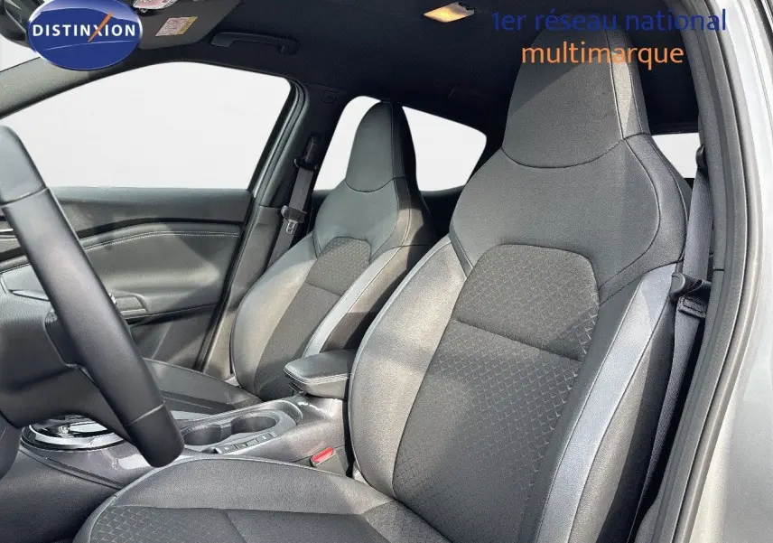 Intérieur du Nissan Juke 2024 montrant les sièges avant en tissu gris avec surpiqûres et accoudoir central.