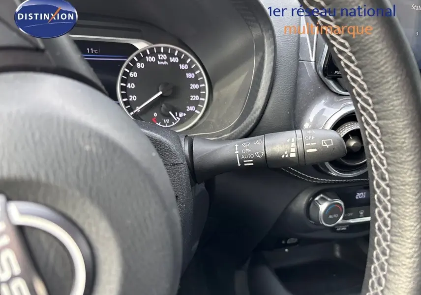 Vue rapprochée du tableau de bord et du volant du Nissan Juke gris perle 2024, avec commandes de phares et climatisation.