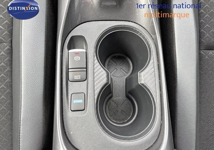 Gros plan sur la console centrale du Nissan Juke 2024 gris perle, montrant porte-gobelets et commandes électroniques.