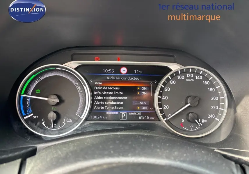 Tableau de bord du Nissan Juke 2024 gris perle, affichant l'écran d'aide au conducteur et compteurs vitesse et énergie.