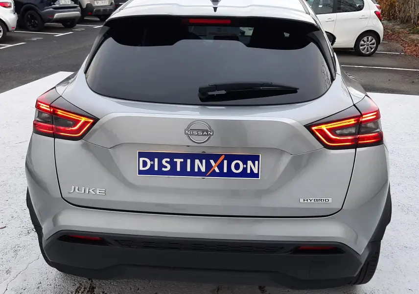 Vue arrière d'un Nissan Juke gris perle métal 2024 avec feux LED allumés et badge Hybrid visible.