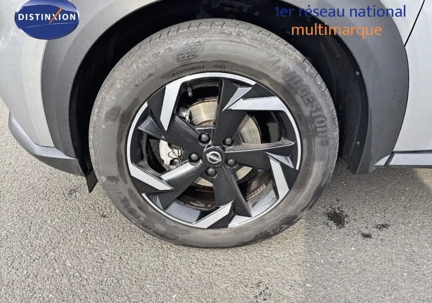 Gros plan sur la roue avant droite du Nissan Juke 2024 gris perle métal avec jante noire et grise au design géométrique.