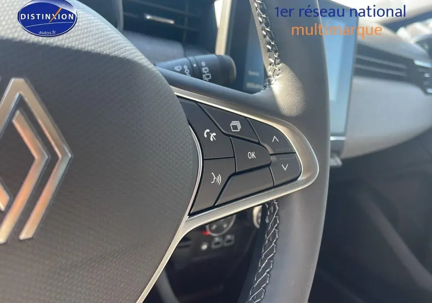 Gros plan sur les commandes du volant multifonction de la Renault Clio V bleu iron, avec écran tactile en arrière-plan.