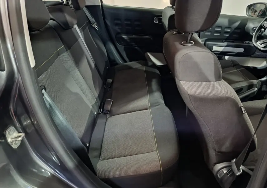 Vue intérieure côté gauche montrant la banquette arrière et les sièges avant noirs de la Citroën C3 gris foncé 2024.