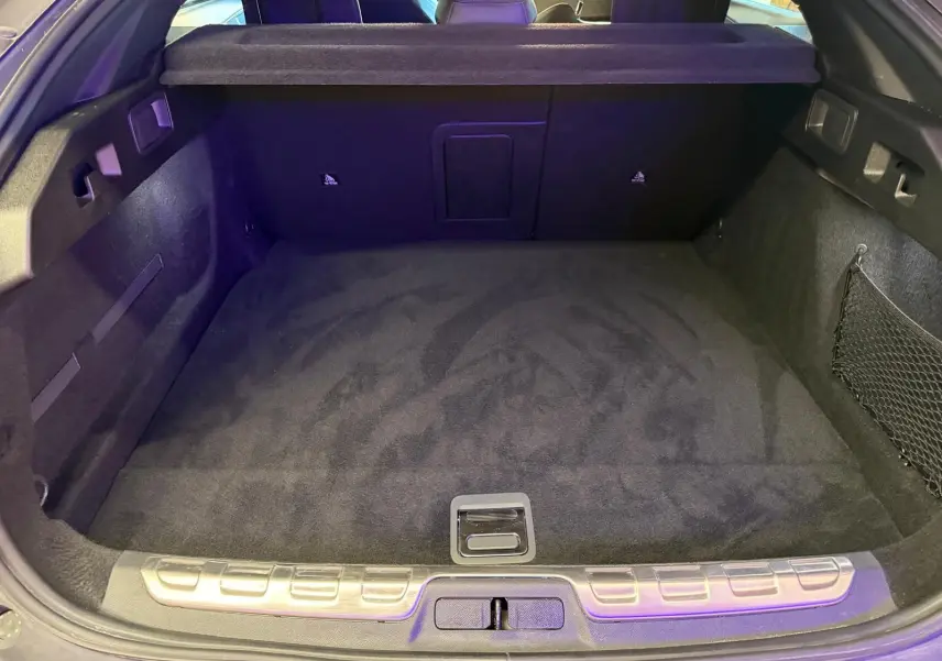 Coffre ouvert vu de l'arrière d'une Peugeot 408 gris, avec tapis de sol noir et filet de rangement latéral.