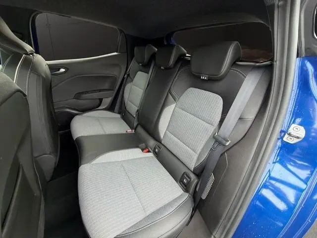 Vue intérieure arrière droite de la Renault Clio Techno E-Tech 2025 bleu, sièges tissu gris et cuir noir avec ceintures visibles.