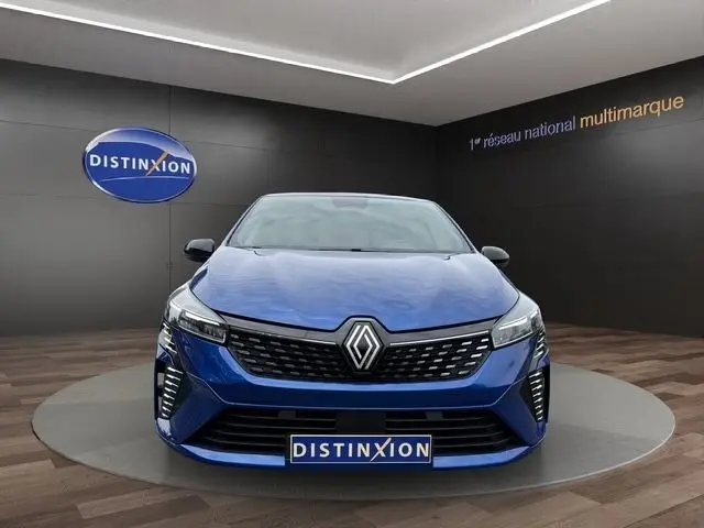 Vue frontale d'une Renault Clio Techno E-Tech full hybrid 2025 en bleu, avec calandre noire et feux LED allumés.
