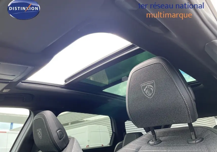 Vue intérieure du Peugeot 5008 Hybrid 2025 montrant les sièges avant en cuir noir avec logo et toit panoramique ouvert.
