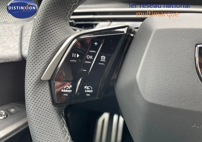 Gros plan sur les commandes au volant du Peugeot 5008 Hybrid 136ch GT, volant cuir perforé noir.