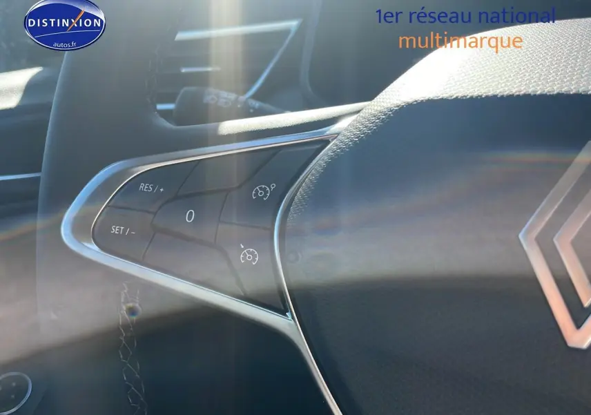 Gros plan sur les commandes du régulateur de vitesse au volant de la Renault Clio V Diesel bleu iron, intérieur lumineux.