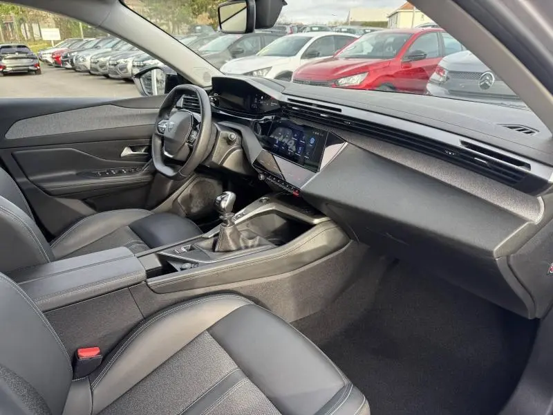 Vue intérieure côté conducteur de la Peugeot 308 2024 avec tableau de bord moderne et boîte manuelle, sièges noirs.
