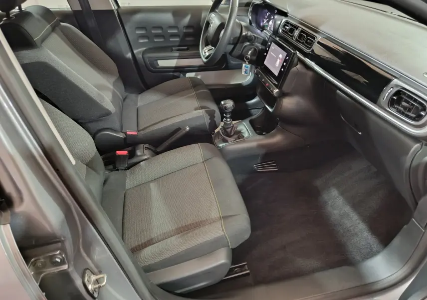Vue intérieure côté conducteur de la Citroën C3 gris clair 2024, montrant sièges tissu, volant multifonctions et écran tactile central.
