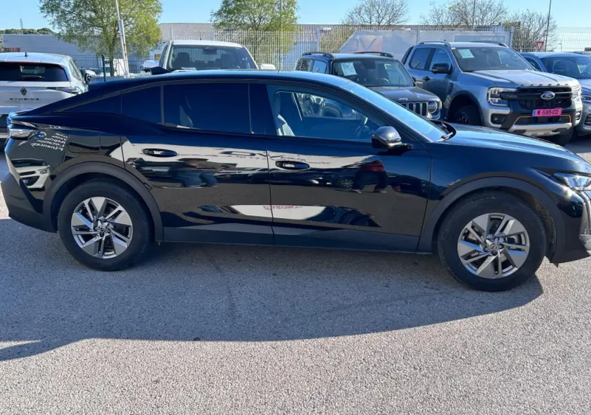 Vue latérale droite d'une Peugeot 408 PHEV 180 e-EAT8 Allure noire avec jantes alliage 17 pouces, stationnée en extérieur.