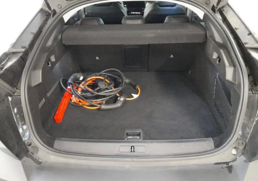 Coffre ouvert vu de l'arrière d'une Peugeot 408 PHEV noire, avec câble de recharge hybride et tapis noir.