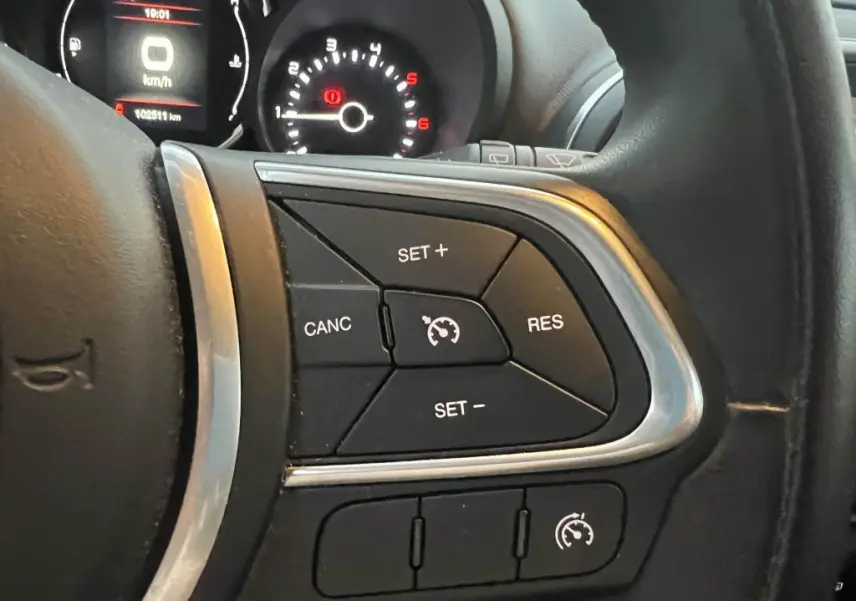 Gros plan sur les commandes du régulateur de vitesse au volant d'une Fiat 500L 2017, tableau de bord en arrière-plan.