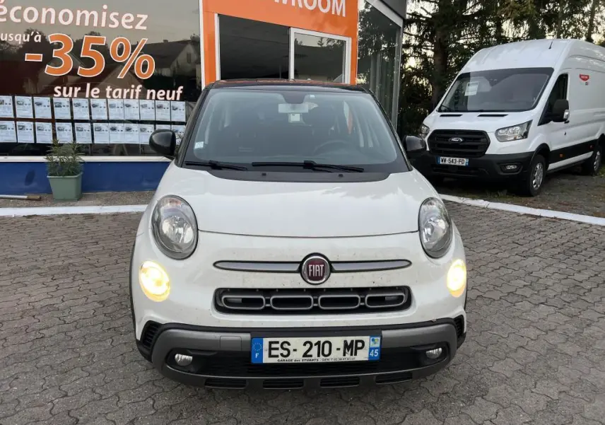 Vue de face d'une Fiat 500L 2017 avec peinture bi-color blanc et toit noir, feux diurnes allumés devant un showroom.