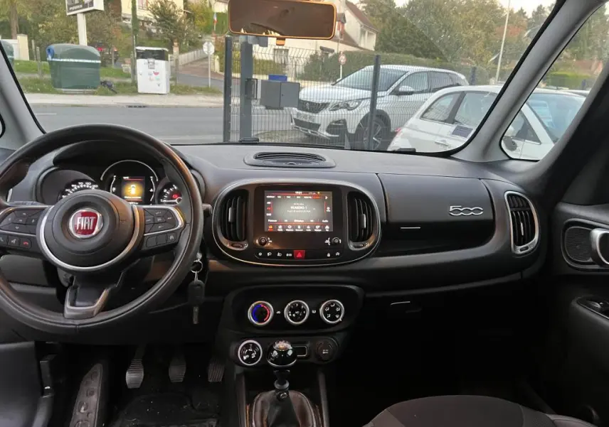 Vue intérieure avant du tableau de bord noir de la Fiat 500L avec volant multifonction et écran tactile central.
