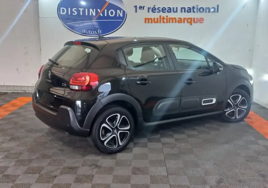 Vue 3/4 arrière droite d'une Citroën C3 noire 2024 avec protections latérales blanches et jantes stylisées.