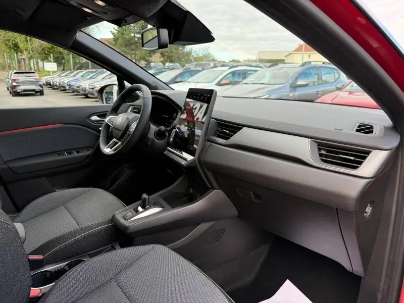 Vue intérieure côté conducteur du Renault Captur 2025 rouge flamme, avec tableau de bord moderne et écran tactile vertical.