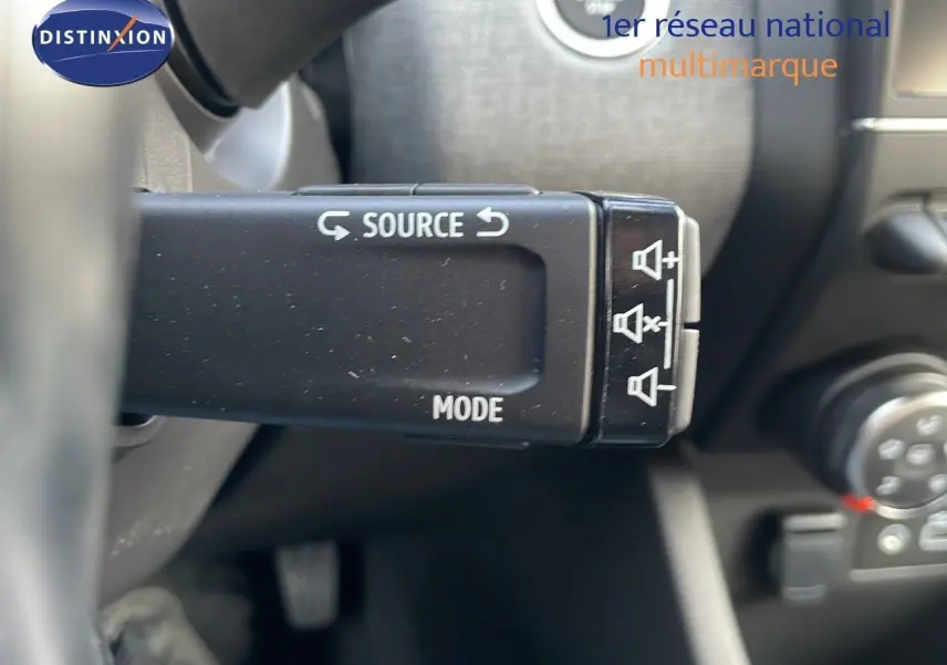 Gros plan sur la commande au volant gauche de la Renault Clio noire étoile métal, montrant les réglages audio et mode source.