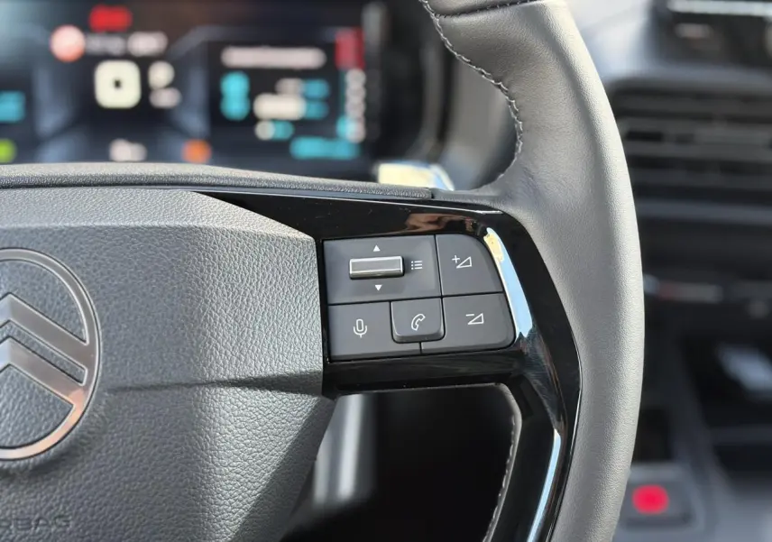 Gros plan sur le volant cuir multifonctions du Citroën Berlingo bleu, avec commandes audio et téléphone intégrées.