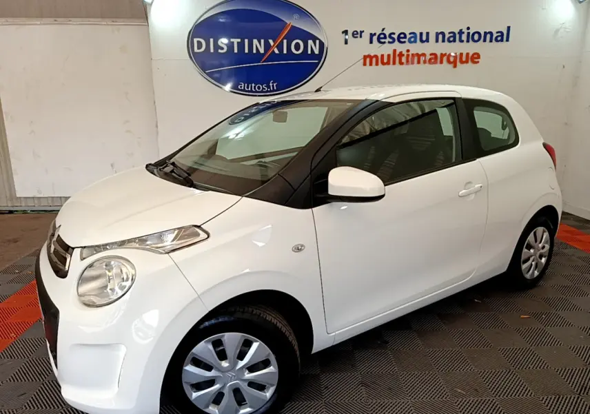 Citroën C1 blanc vue 3/4 avant droit en intérieur, avec jantes acier et rétroviseurs blancs.