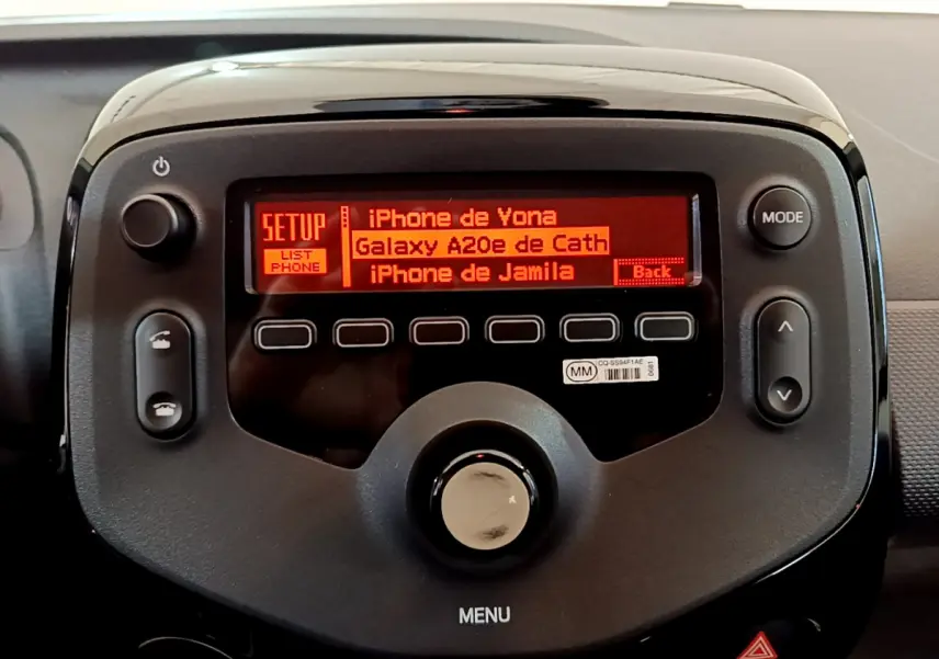 Gros plan sur l’écran central noir de la Citroën C1 blanc, affichant la liste des téléphones connectés en rouge.