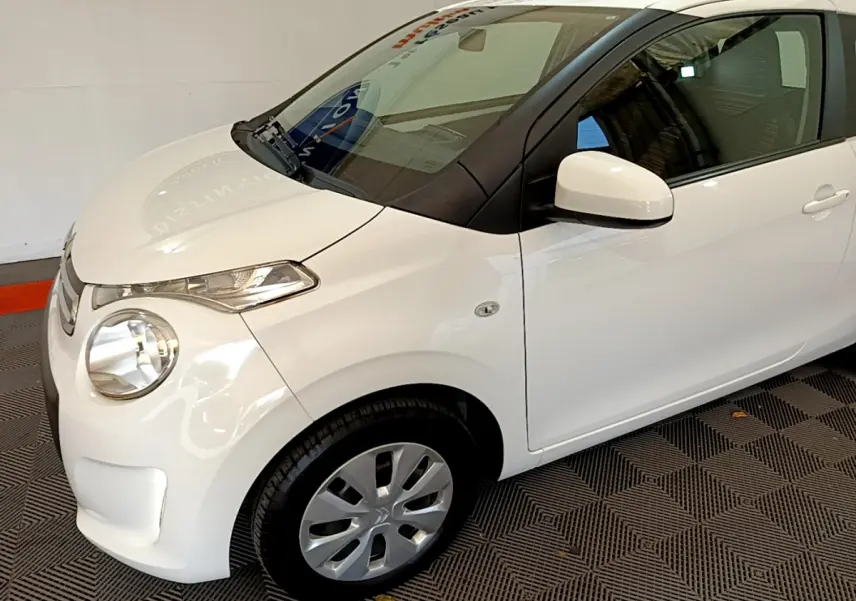 Vue 3/4 avant droit d'une Citroën C1 blanche 2020 avec phares ellipsoïdaux et rétroviseurs peints assortis.