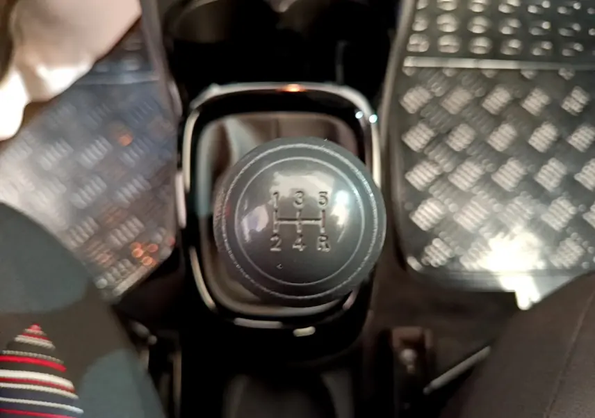 Gros plan sur le levier de vitesses manuel noir de la Citroën C1 blanche, entouré des sièges avant et tapis métallisés.