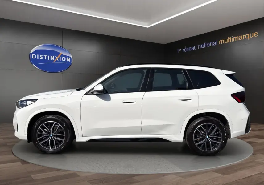 Vue arrière d'un BMW X1 blanc sDrive20d M SPORT avec diffuseur noir et feux LED distinctifs.