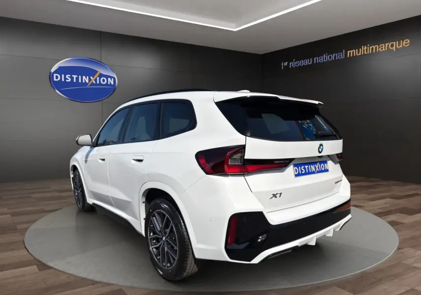 BMW X1 sDrive20d blanc en 3/4 arrière droit avec toit noir et jantes sport dans showroom