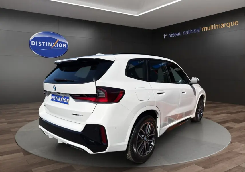BMW X1 sDrive20d blanc vue 3/4 avant droite avec calandre noire et jantes foncées en showroom