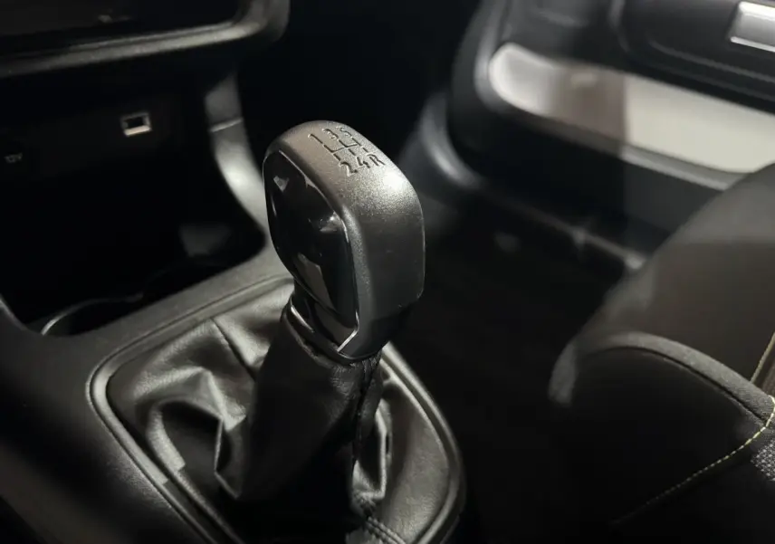 Gros plan sur le levier de vitesses manuel noir de la Citroën C3 PureTech 82, intérieur sombre avec coutures visibles.