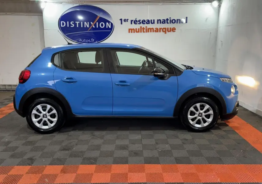 Vue de profil côté gauche d'une Citroën C3 bleu vif avec jantes argentées dans un showroom intérieur.